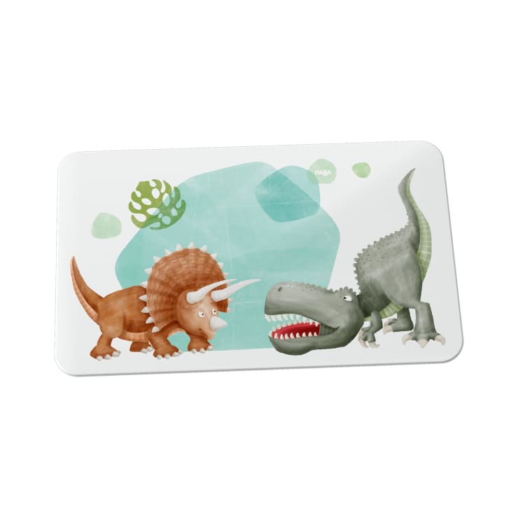Eine rechteckige Matte zeigt Cartoon-Abbildungen eines braunen Triceratops und eines grünen Tyrannosaurus Rex, die sich gegenüberstehen, mit abstrakten grünen Formen im Hintergrund.