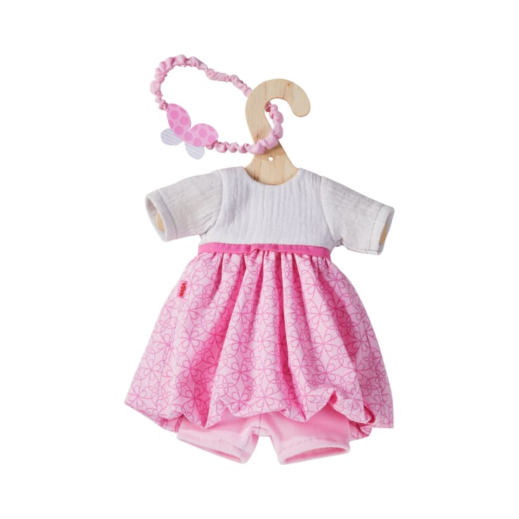 Ein kleines rosafarbenes und weißes Puppenkleid mit einem passenden rosafarbenen Stirnband, ausgestellt auf einem hölzernen Kleiderbügel, vor einem weißen Hintergrund.
