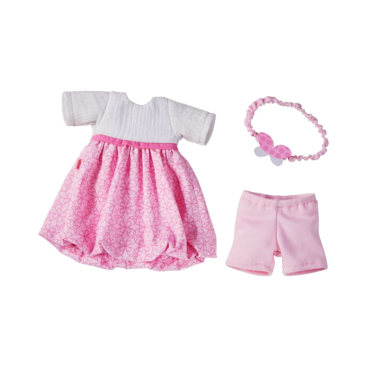 Ein Puppen-Outfit-Set mit einem weiß-rosa Kleid mit gemustertem Rock, einem Paar hellrosa Shorts und einem passenden rosa Stirnband mit einer Schleife auf weißem Hintergrund.