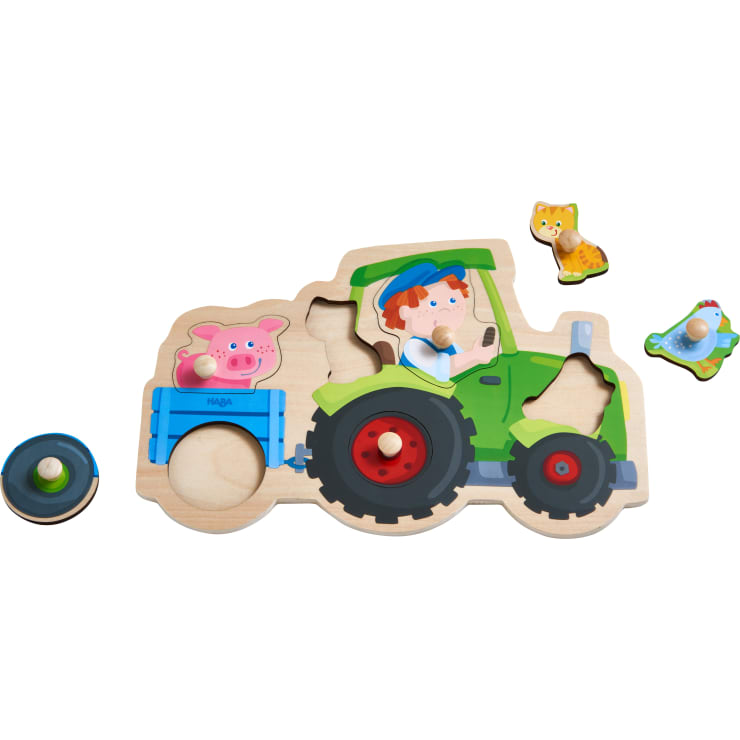 Ein Holzpuzzle, das einen grünen Traktor mit einem blauen Anhänger darstellt, der von einem Bauern gefahren wird. Zu den Puzzleteilen gehören ein Schwein, eine Katze, ein Vogel und ein rundes Rad, alle mit kleinen Holzknöpfen für eine einfache Handhabung.