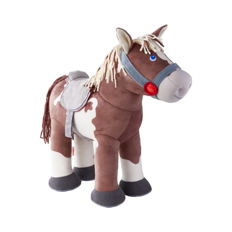 Ein braunes und weißes Plüschpferd mit grauem Sattel, grauen Zügeln, einem roten, kreisförmigen Detail in der Nähe des Mauls, blauen Augen und beigefarbener Mähne und Schweif, auf weißem Hintergrund.