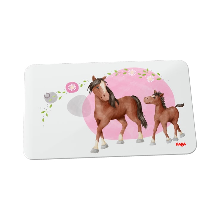 Ein rechteckiges Tischset mit einer Illustration von zwei braunen Pferden, die auf einem rosa Kreis stehen. Im Hintergrund sind Blumen, Blätter und ein kleiner Vogel auf einem Zweig zu sehen. Das HABA-Logo befindet sich in der unteren rechten Ecke.