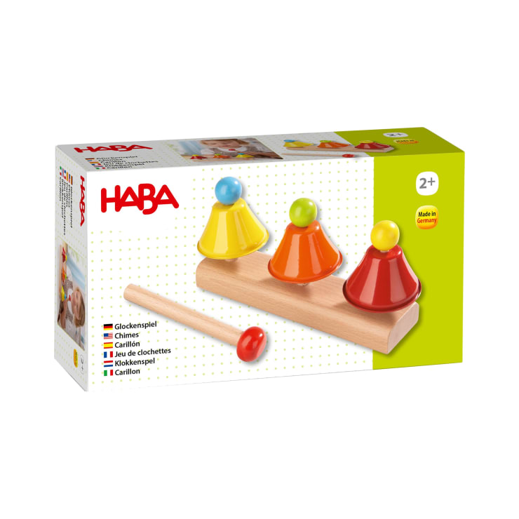 Eine Schachtel mit HABA-Spielzeugglocken für Kinder ab 2 Jahren mit drei bunten Glockenspielen auf einem Holzsockel und einem Holzhammer. Die Verpackung zeigt rote, gelbe und orangefarbene Glockenspiele mit blauen, gelben und orangen Knöpfen.