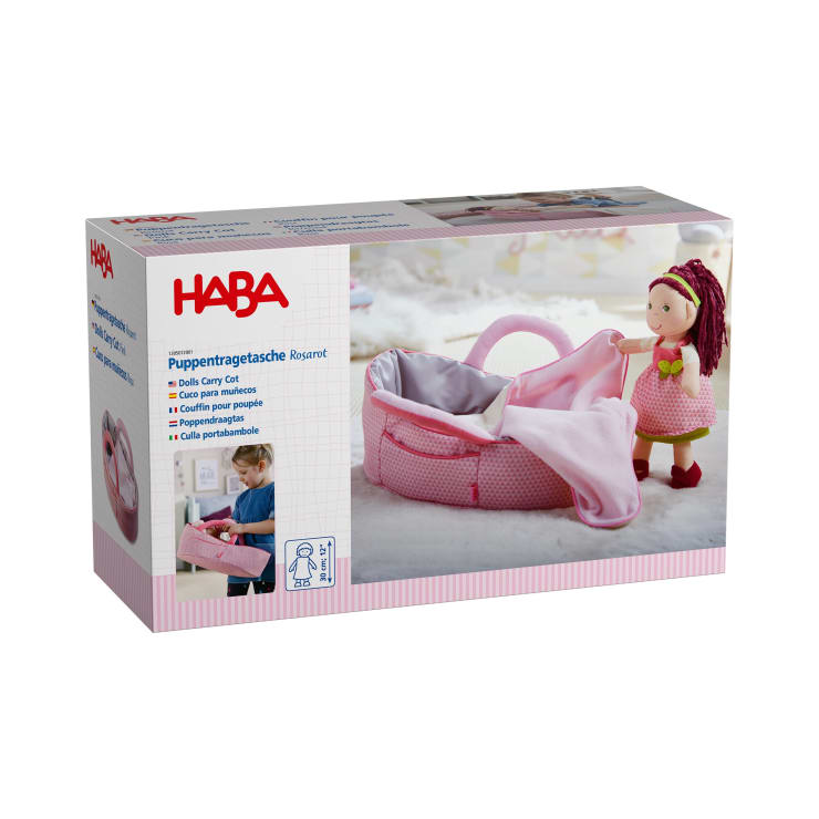 Schachtel für ein HABA-Puppentragebett mit einem Foto eines rosafarbenen Spielzeugbettes und einer Puppe, Produktdetails in mehreren Sprachen und Bildern eines Kindes, das mit dem Bettchen spielt und einer Puppe, die daneben steht.