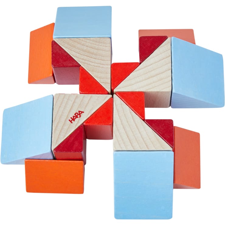 Eine geometrische Anordnung von Holzspielzeugblöcken in Rot, Orange, Blau und natürlichen Holzfarben, die ein symmetrisches, pinradähnliches Muster bilden. Die Blöcke bestehen aus Würfeln und Dreiecken. Auf einem Block ist das Wort HABA aufgedruckt.