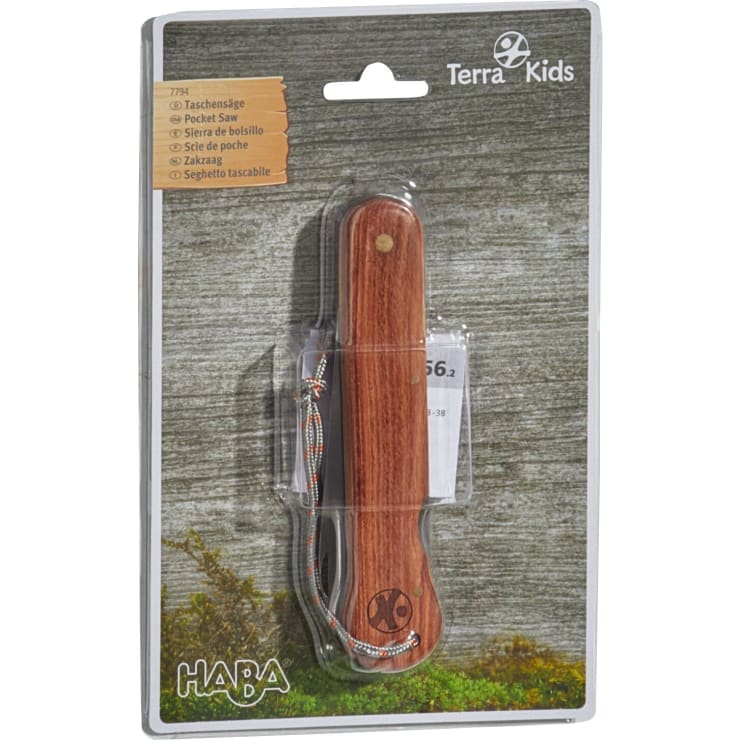 Eine verpackte HABA Terra Kids Taschensäge mit Holzgriff und geflochtenem Schlüsselband vor einem strukturierten grau-grünen Hintergrund. Die Produktdetails sind in mehreren Sprachen auf der Verpackung aufgedruckt.