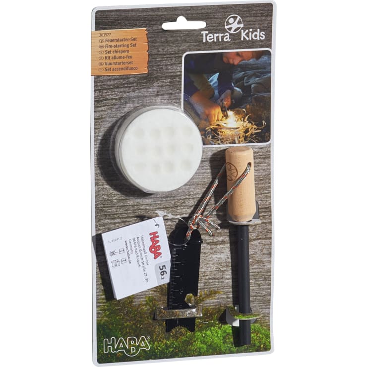 Ein verpacktes Terra Kids Anzündset von HABA. Das Set besteht aus einem runden Wattebausch, einem Feuerstarter mit Holzgriff und Anzünder, einem Lineal und einer Anleitung, die auf einer Pappunterlage abgebildet ist.