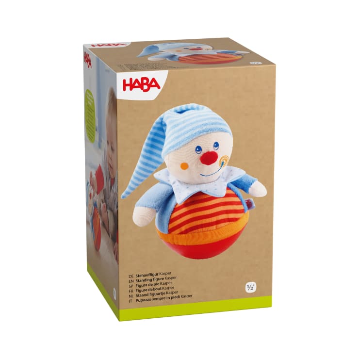 Eine Schachtel mit einem HABA-Stofftier mit einer clownähnlichen Figur, die einen blauen Hut und ein gestreiftes Hemd trägt. Die Verpackung zeigt das Spielzeug und enthält Produktinformationen in mehreren Sprachen.