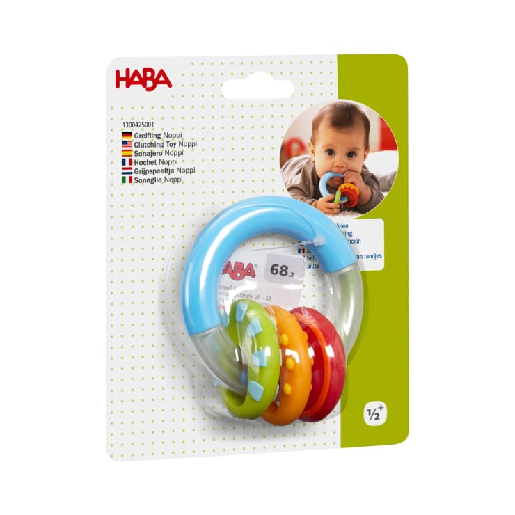 Ein Baby hält einen blauen und bunten Beißring in seinem Mund. Der Beißring ist auf einer grün-weißen Karte mit dem HABA-Logo verpackt und enthält Produktinformationen in mehreren Sprachen.