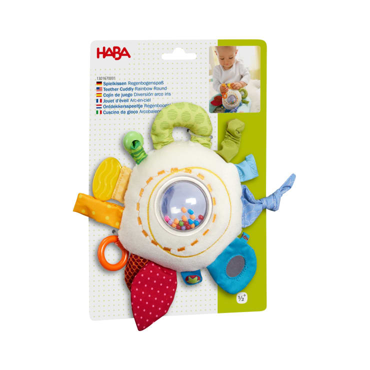 Ein verpacktes HABA-Baby-Sinnesspielzeug mit bunten Stoffanhängern, knisternden Elementen, einem Spiegel und einer durchsichtigen Mitte, die mit bunten Perlen gefüllt ist. Die Verpackung enthält Produktinformationen und ein Foto eines Babys.