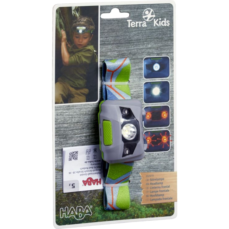 Eine verpackte Terra Kids Stirnlampe von HABA mit grauem und grünem Design und verstellbarem Band. Auf der Verpackung sind Produktbilder und ein Foto eines Kindes, das die Stirnlampe auf der Stirn trägt, abgebildet.