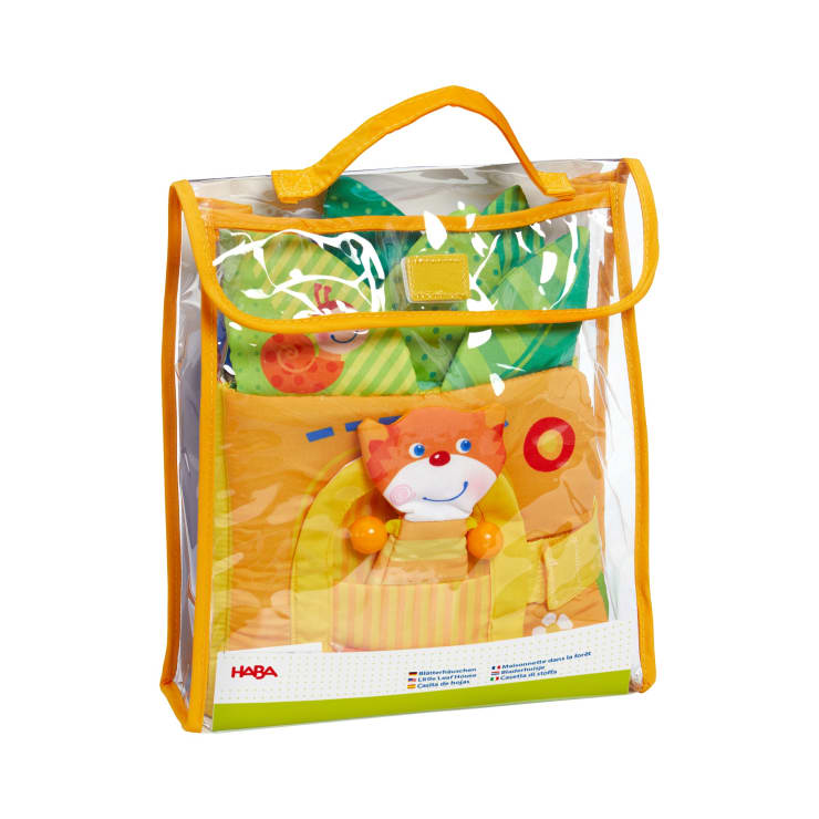 Eine transparente Plastiktüte mit gelbem Rand und Griff enthält ein farbenfrohes, weiches Babyspielzeug mit einem lächelnden Katzengesicht. Das HABA-Logo ist in der rechten unteren Ecke der Verpackung zu sehen.