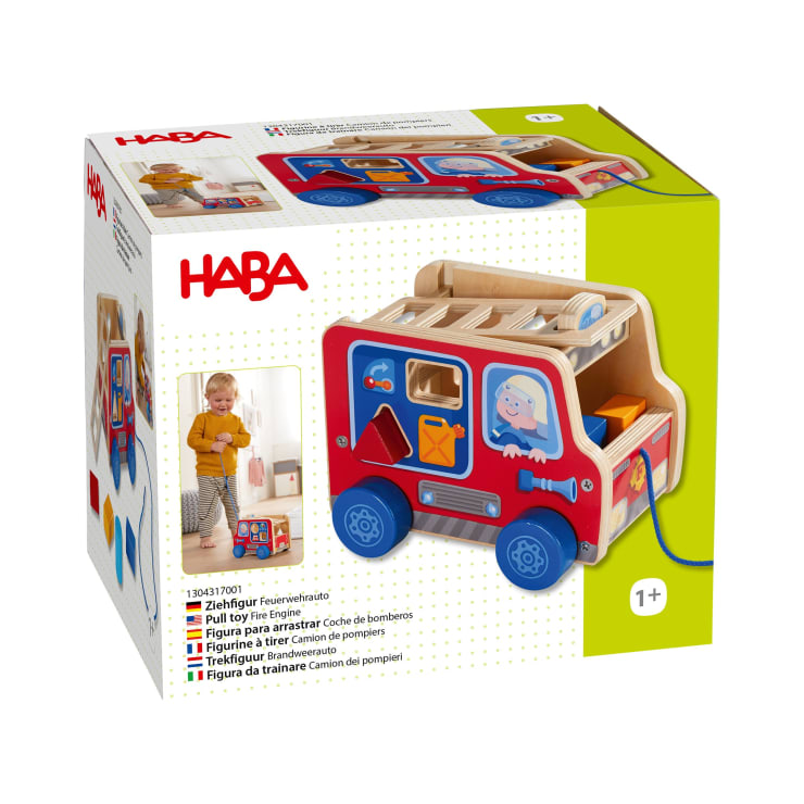 Eine Schachtel mit einem Holzspielzeug der Marke HABA in Form eines Feuerwehrautos mit bunten Details und Ausschnitten. Die Schachtel zeigt das Spielzeug und ein Kind, das damit spielt. Das Spielzeug wird für das Alter von 1 Jahr und älter empfohlen.