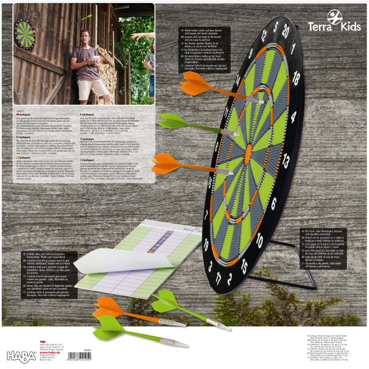Ein Mann wirft einen Dartpfeil auf eine große, runde, schwarz-grüne Dartscheibe, in der orangefarbene und grüne Pfeile stecken. In der Nähe liegt auf einer hölzernen Unterlage ein Spielberichtsbogen mit einem Bleistift und drei Pfeilen. Das Branding von Terra Kids ist sichtbar.