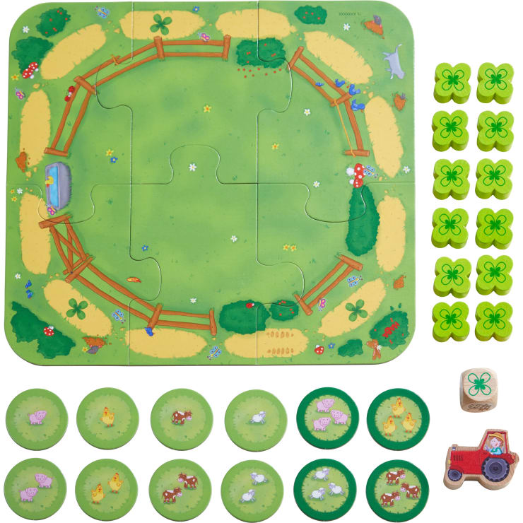Ein Tischspiel mit einem grünen kreisförmigen Spielbrett, das in vier Puzzleteile unterteilt ist, zwanzig grünen Spielsteinen mit Kleesymbolen, acht Tierplättchen, einem roten Spielzeugtraktor und einem Holzwürfel mit einem Kleebild.