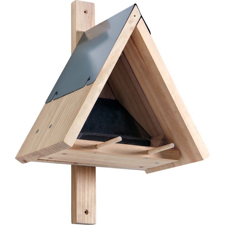 Ein hölzerner Fledermauskasten mit dreieckigem Grundriss, der auf einem senkrechten Holzpfosten montiert ist, hat ein Metalldach und zwei hölzerne Stege am Eingang.
