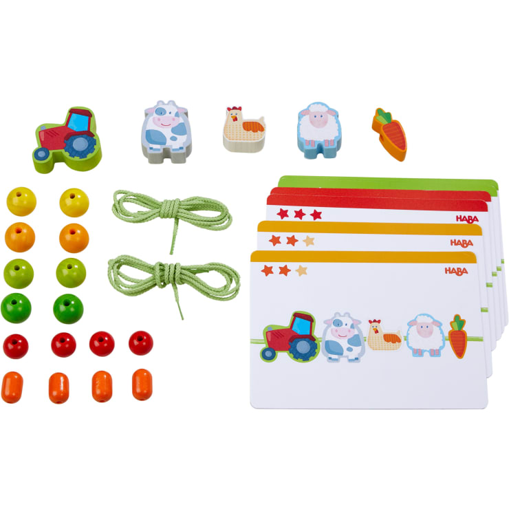 Ein Set mit farbenfrohen Spielfiguren, darunter ein Traktor, eine Kuh, ein Schaf, ein Huhn, Karotten, Holzperlen in verschiedenen Farben, zwei grüne Schnüre und mehrere illustrierte Karten mit Sternebewertungen und HABA-Branding.