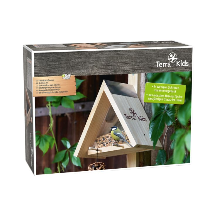 Rechteckige Schachtel eines Terra Kids Vogelfutterspender-Bausatzes mit der Abbildung eines dreieckigen hölzernen Vogelfutters mit Vogelfutter und einem Vogel vor einem Holzzaun und grünem Laub. Der Text auf der Verpackung ist in Deutsch.