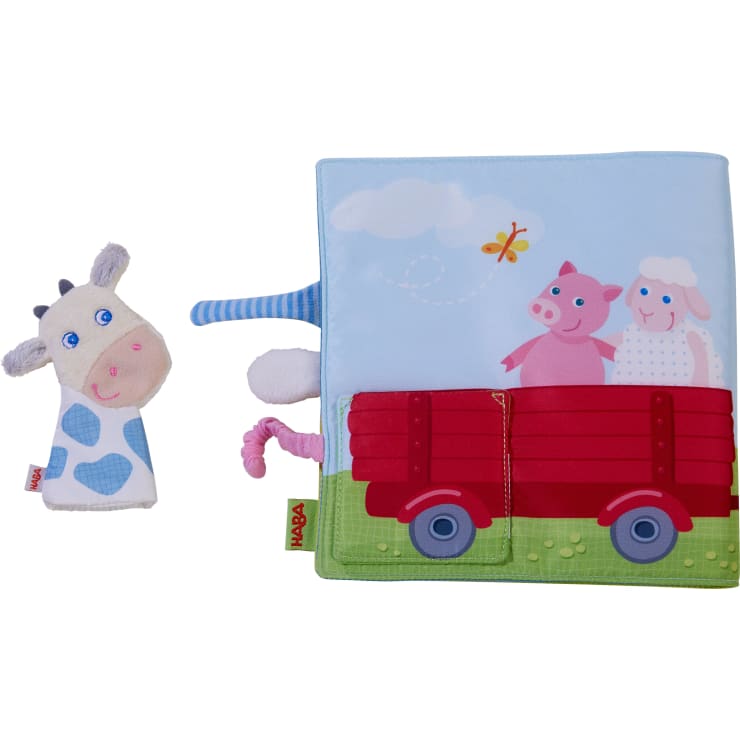 Ein Kinderbuch aus Stoff mit einem roten Wagen, auf dem ein Schwein und ein Schaf abgebildet sind, und einer Kuh-Fingerpuppe aus Plüsch. Das Buch ist mit Registerkarten und Bauernhofmotiven versehen, und beide Artikel sind aus weichem Material gefertigt.