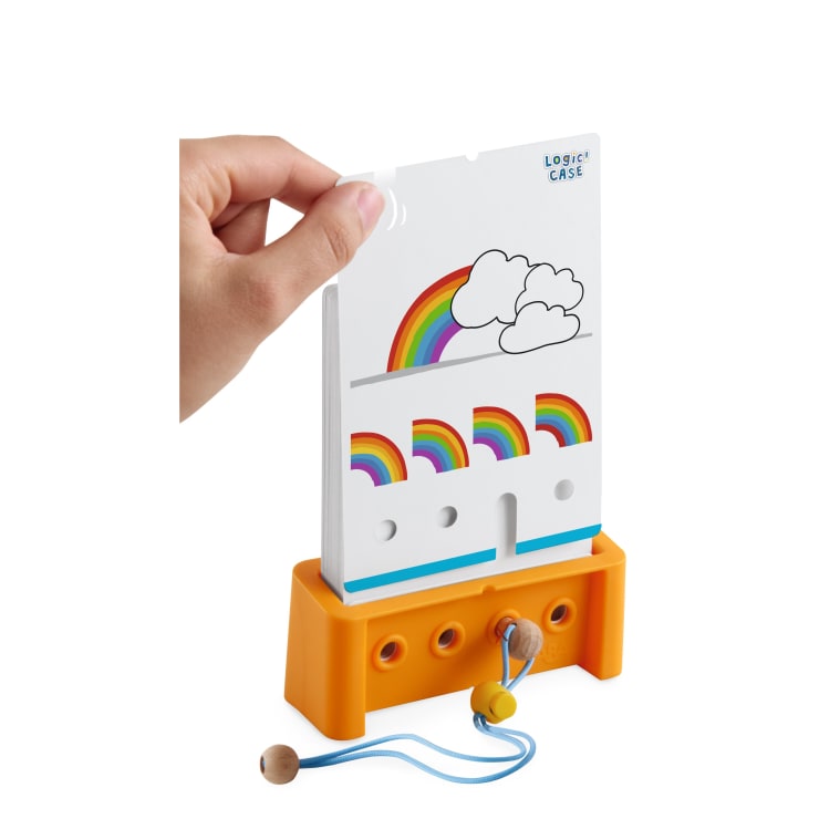 Eine Hand steckt eine Karte mit Regenbögen in einen orangefarbenen Ständer von Logic CASE. Die Karte zeigt ein Puzzle mit teilweisen Regenbögen und Wolken, und ein Zeiger mit einer Schnur ist an dem Ständer befestigt.