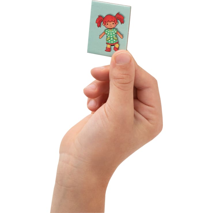 Eine Hand hält eine kleine rechteckige Karte mit der Abbildung eines Mädchens mit roten Zöpfen, das ein grünes Kleid mit weißen Punkten und rote Schuhe trägt.