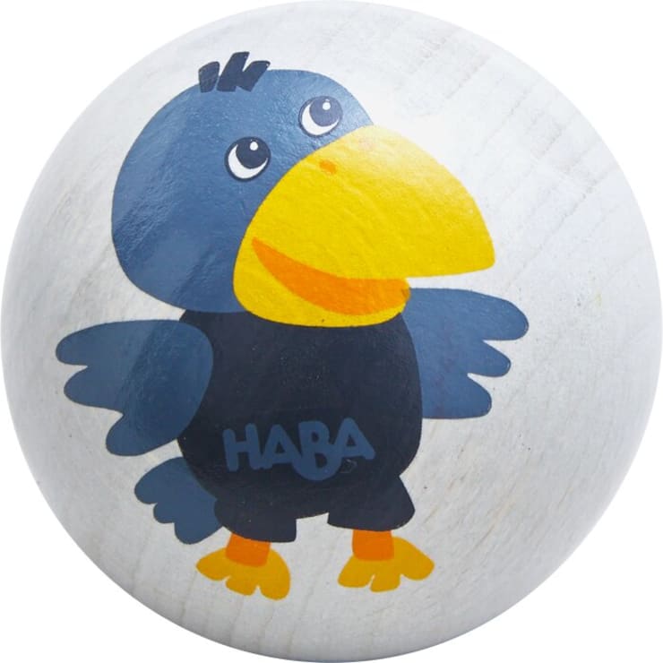 Eine weiße Holzkugel mit der Illustration eines lächelnden Cartoon-Vogels mit blauen Flügeln, einem großen gelben Schnabel, orangefarbenen Füßen und dem Wort "HABA" auf der Brust.