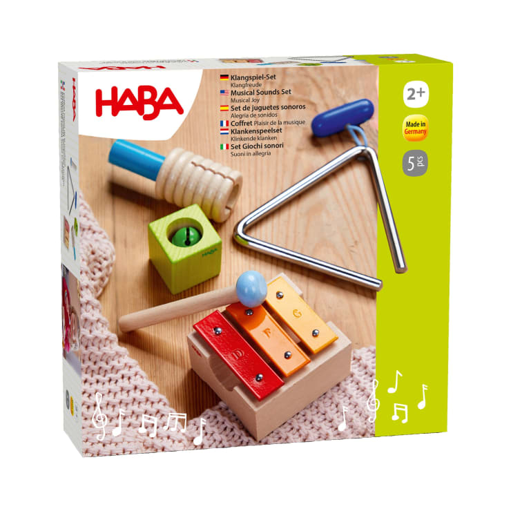 Eine Schachtel mit einem HABA Musikalische Klänge Set für Kinder ab 2 Jahren mit Xylophon, Triangel, Guiro und Glocke; die Verpackung ist weiß mit roten und gelben Akzenten und Produktbildern auf der Vorderseite.