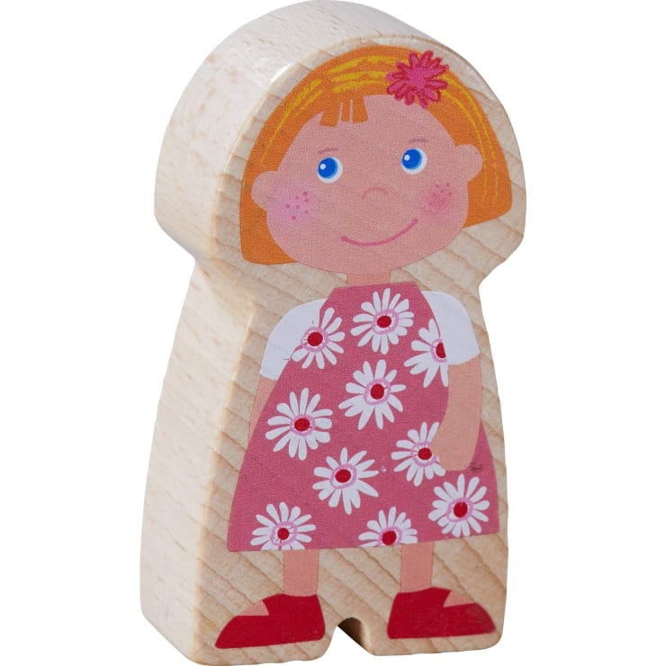 Holzspielzeugfigur eines Mädchens mit kurzen blonden Haaren, das ein rosa Kleid mit weißen Gänseblümchen, rote Schuhe und eine rosa Blume im Haar trägt. Die Figur ist auf einen glatten, hellen Holzblock gemalt.