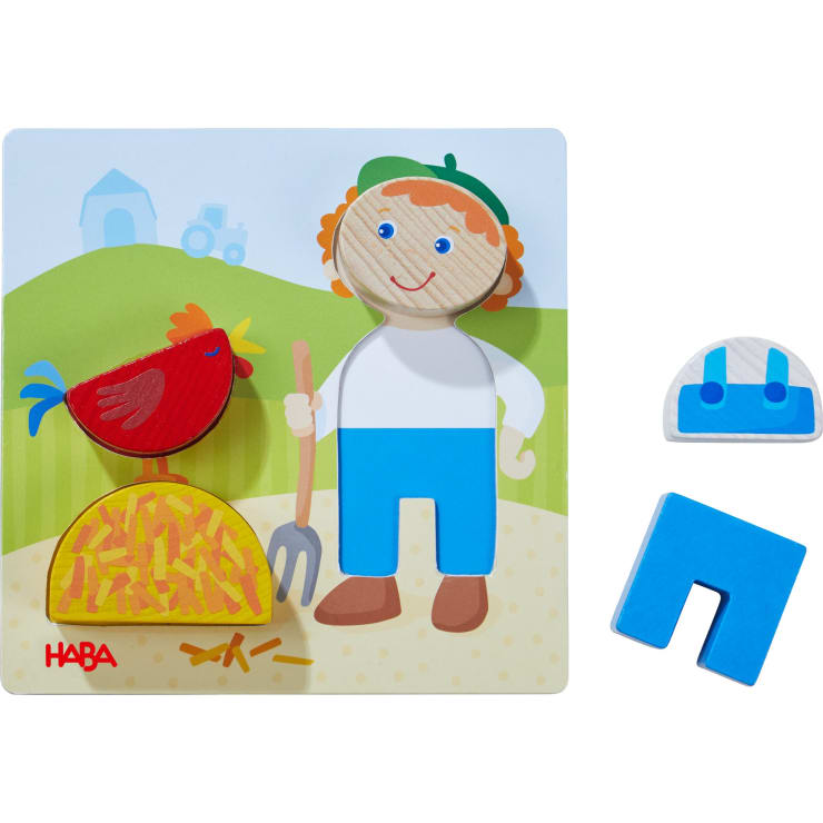 Ein Holzpuzzle zeigt einen Bauern, ein rotes Huhn, einen Heuhaufen und eine Mistgabel vor einem Bauernhofhintergrund. Zwei Puzzleteile - ein blauer Overall und ein blauer U-förmiger Block - befinden sich auf der rechten Seite des Puzzles.
