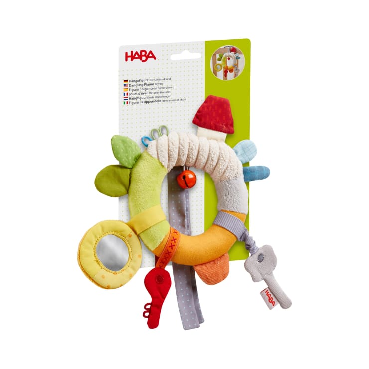 Ein farbenfrohes HABA-Babyspielzeug mit verschiedenen Strukturen, einem Spiegel, einer kleinen roten Glocke, Stoffanhängern und weichen Formen, ausgestellt auf der Originalverpackung vor einem weißen Hintergrund.