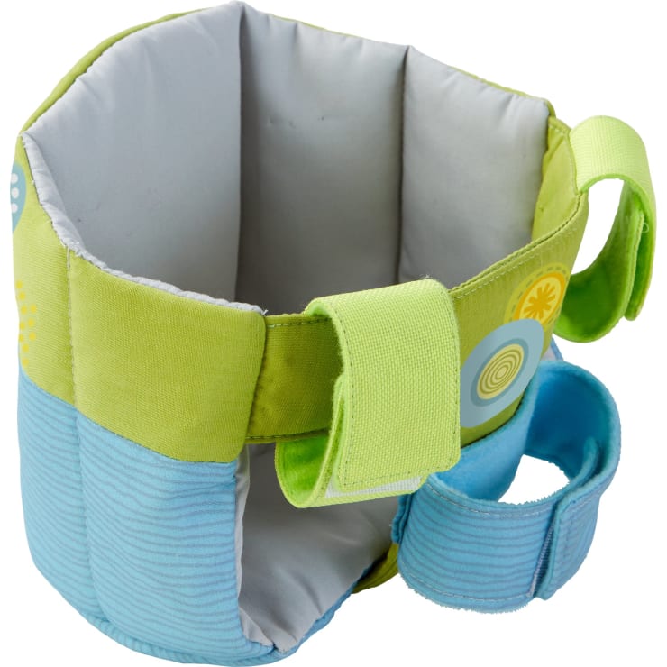 Ein weicher, gepolsterter Stoffsitz in hellgrünen und blauen Farben mit kreisförmigen Mustern, mit zwei seitlichen Griffen und einem verstellbaren Riemen vorne. Der Sitz scheint für Säuglinge und Kleinkinder geeignet zu sein.