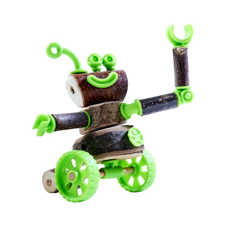 Ein kleiner Spielzeugroboter aus Holzteilen und hellgrünen Kunststoffteilen, darunter Räder, Arme, Augen und ein lächelnder Mund, ist mit einem Arm angehoben und mit leicht geneigtem Kopf zu sehen.