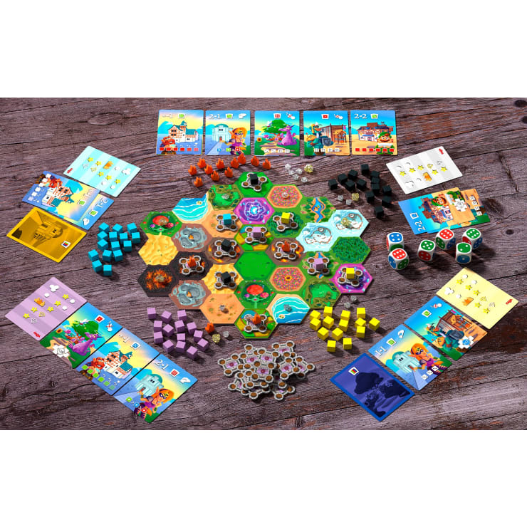 Ein farbenfrohes Brettspiel wird auf einer Holzfläche aufgebaut. Sechseckige Kacheln bilden einen zentralen Spielplan, umgeben von Karten, Würfeln, Spielsteinen, Würfeln in verschiedenen Farben und einzelnen Spielertafeln, die ordentlich um den Spielplan herum angeordnet sind.