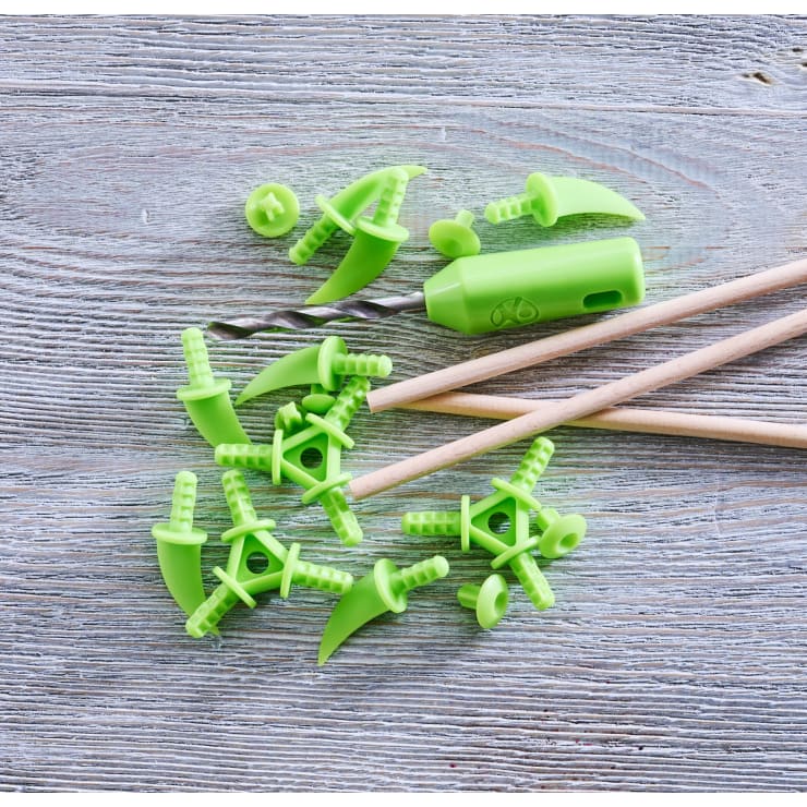 Grüne Strickwerkzeuge aus Kunststoff und ein passender Griff sind auf einer hellen Holzfläche neben zwei Holzstricknadeln angeordnet.