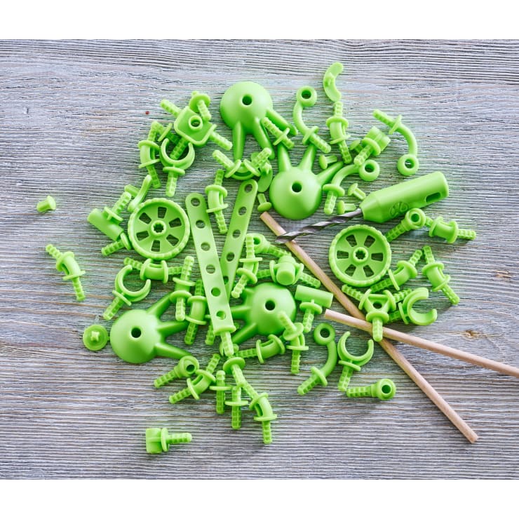 Grüne Plastikspielzeugteile und zwei Holzstäbe sind auf einer hellen Holzoberfläche verstreut. Zu den Teilen gehören Zahnräder, Stangen, Verbindungsstücke und verschiedene andere Formen.
