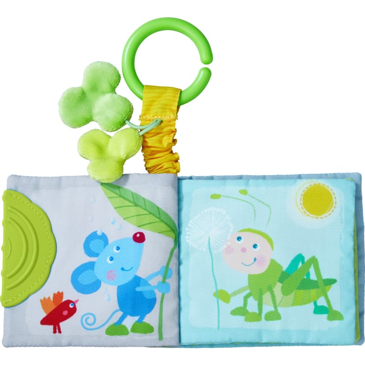 Ein weiches Babybuch aus Stoff mit Illustrationen von einer blauen Maus, die ein Blatt hält, einem roten Vogel und einem grünen Grashüpfer mit Löwenzahn. Das Buch hat eine grüne Zahnecke und einen Plastikring mit drei grünen Plüschfiguren daran.