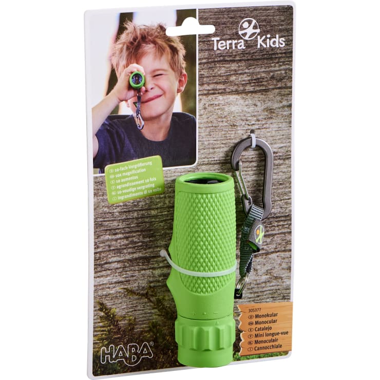 Ein verpacktes HABA Terra Kids Monokular in Grün mit Handschlaufe und Karabiner. Die Verpackung zeigt ein Foto eines lächelnden Kindes, das durch das Monokular schaut. Der Text hebt die 10-fache Vergrößerung in mehreren Sprachen hervor.