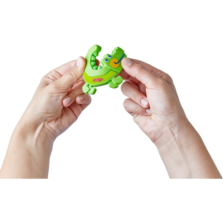Zwei Hände halten ein kleines grünes Plastikspielzeug in Form eines Krokodils, auf dem das Wort Happy aufgedruckt ist, vor einem weißen Hintergrund.