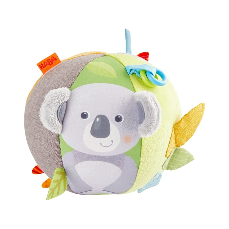Ein weicher Stoffball mit einer niedlichen Koala-Illustration, strukturierten Elementen, farbenfrohen Stoffanhängern und einem blauen Kunststoffring, der als sensorisches Spielzeug für Babys oder Kleinkinder konzipiert ist.