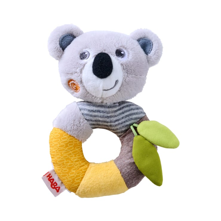 Eine Plüsch-Koala-Baby-Rassel mit grauem Kopf, schwarzer Nase, runden Ohren und gestreiftem Hals. Der ringförmige Körper hat gelbe, braune und grüne Segmente mit zwei Stoffblättern und einem "HABA"-Anhänger.