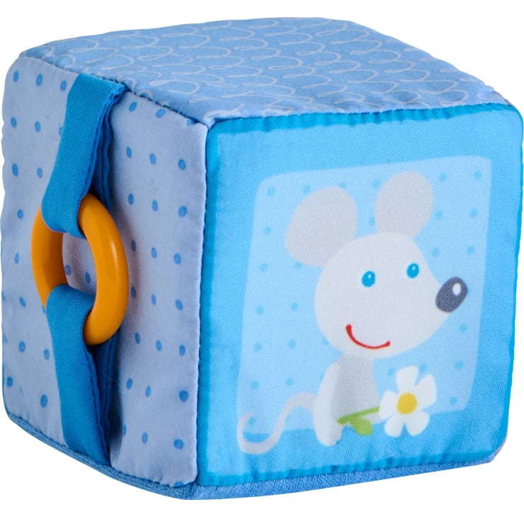Ein weicher, blauer Stoffspielzeugblock mit kleinen Tupfen, einem gelben Plastikring und der Abbildung einer lächelnden weißen Maus, die auf einer Seite eine Blume hält.