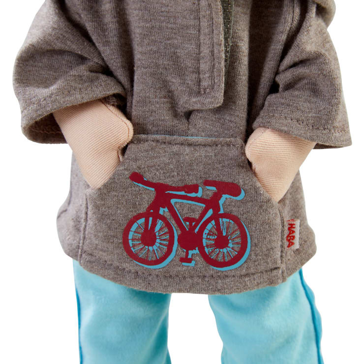 Eine Puppe, die einen grauen Kapuzenpullover mit einer roten Fahrradgrafik auf der Vordertasche und eine hellblaue Hose trägt, wobei beide Hände in die Kapuzentasche gesteckt sind.