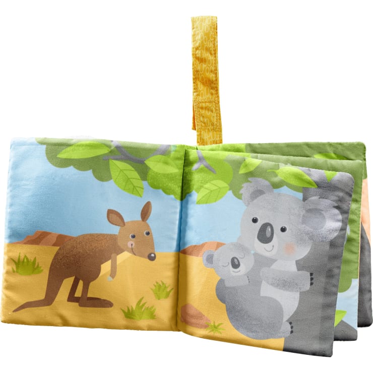 Ein Kinderbuch aus weichem Stoff zeigt auf einer Seite ein Känguru und auf der gegenüberliegenden Seite einen Koala mit einem Koala-Baby auf einem Baum. Oben ist eine gelbe Schleife angebracht.