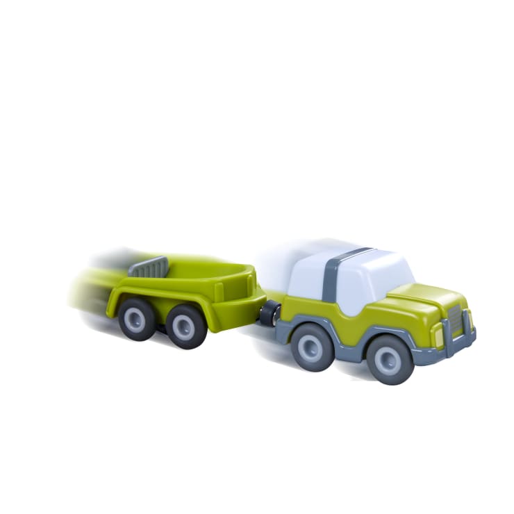 Ein grün-weißer Spielzeugtruck mit grauem Streifen zieht einen passenden grünen Anhänger; beide sind in Bewegung mit Unschärfeeffekten auf der linken Seite zu sehen.