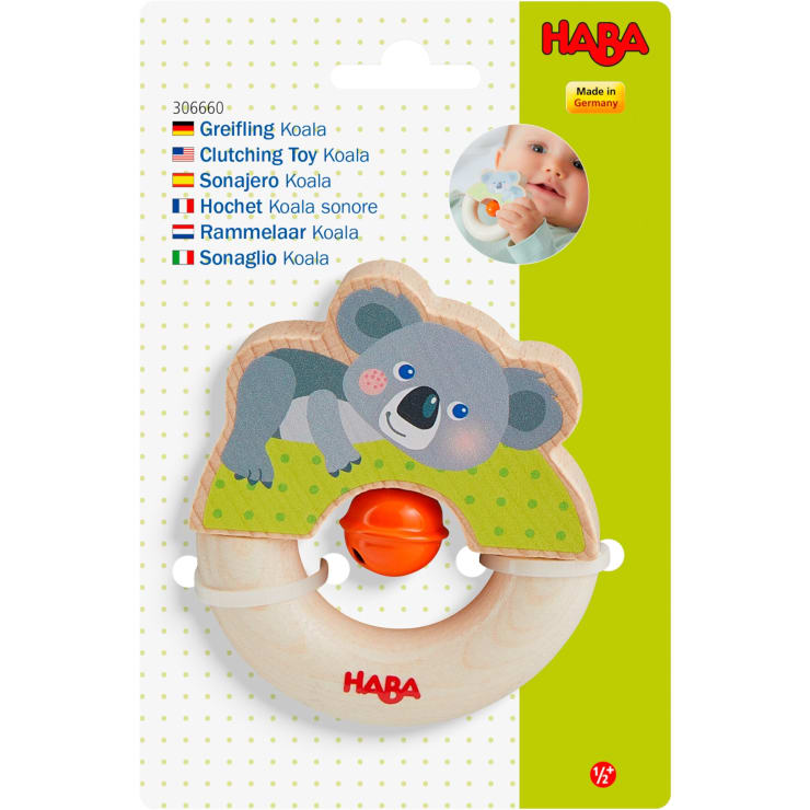 In der Verpackung ist ein hölzernes Greifspielzeug mit einem Cartoon-Koala-Motiv und einem orangefarbenen Kunststoffring in der Mitte abgebildet. Auf der Verpackung sind Produktinformationen und das Bild eines Babys, das das Spielzeug hält, abgebildet.