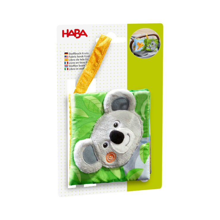 Ein weiches Stoffbuch für Babys mit einem Plüsch-Koala-Gesicht auf dem Einband, grünem Blätterhintergrund, gelber Stoffschlaufe zum Aufhängen und einer Verpackung mit dem HABA-Logo und mehrsprachigen Produktbeschreibungen.