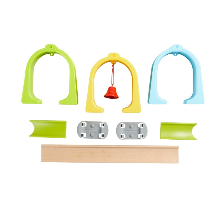 Plastikspielzeugteile in Grün, Gelb und Blau, eine kleine rote Glocke, vier graue Befestigungsteile, zwei grüne gebogene Stützen und eine Holzstange auf weißem Hintergrund.