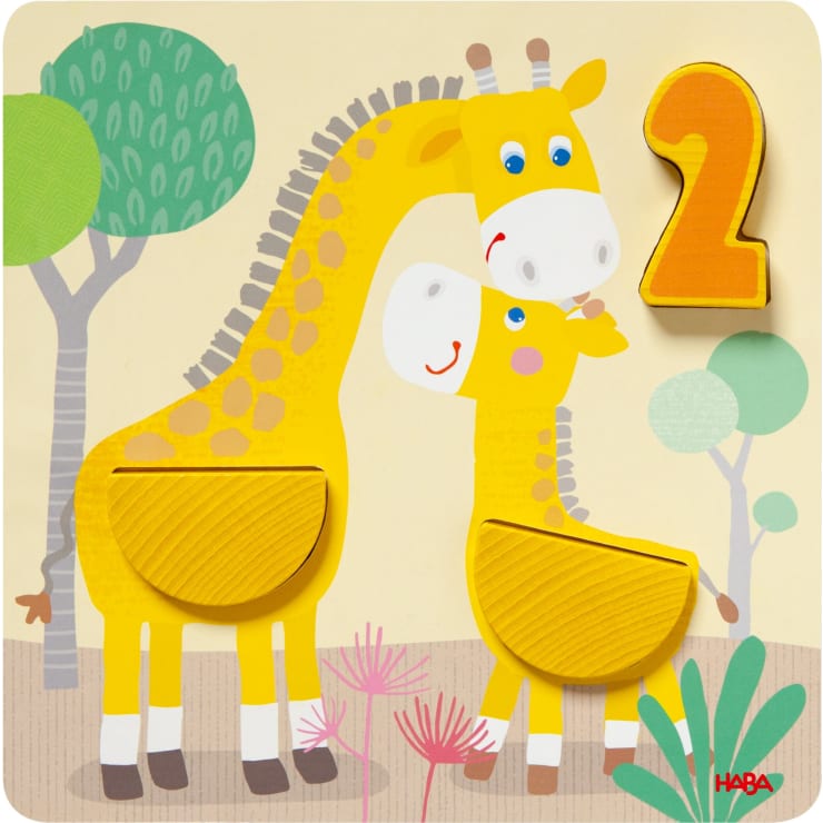 Ein Holzpuzzle zeigt zwei Cartoon-Giraffen, eine Erwachsene und ein Baby, mit einer großen gelben Zahl 2 auf der rechten Seite. Im Hintergrund sind Bäume und Pflanzen abgebildet. Der Markenname HABA erscheint in der unteren rechten Ecke.