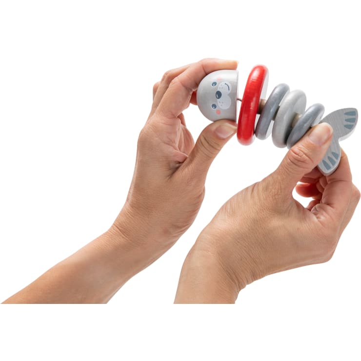 Zwei Hände halten ein hölzernes Stapelspielzeug in Form eines Tieres mit weißem Boden, roten und grauen Ringen und einem kleinen Schwanz. Der Hintergrund ist weiß.