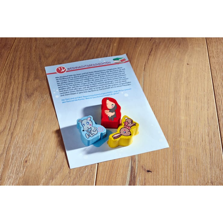 Ein Blatt Papier mit deutschem Text und einem illustrierten Mädchen in einem roten Mantel liegt auf einer Holzfläche. Drei bunte, tierförmige Spielsteine - eine blaue Maus, ein gelber Hase und eine rosa Biene - sind auf dem Papier platziert.